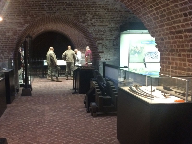 A room inside the Harbor Defense Museum with brick flooring and walls with several exhibits on display.